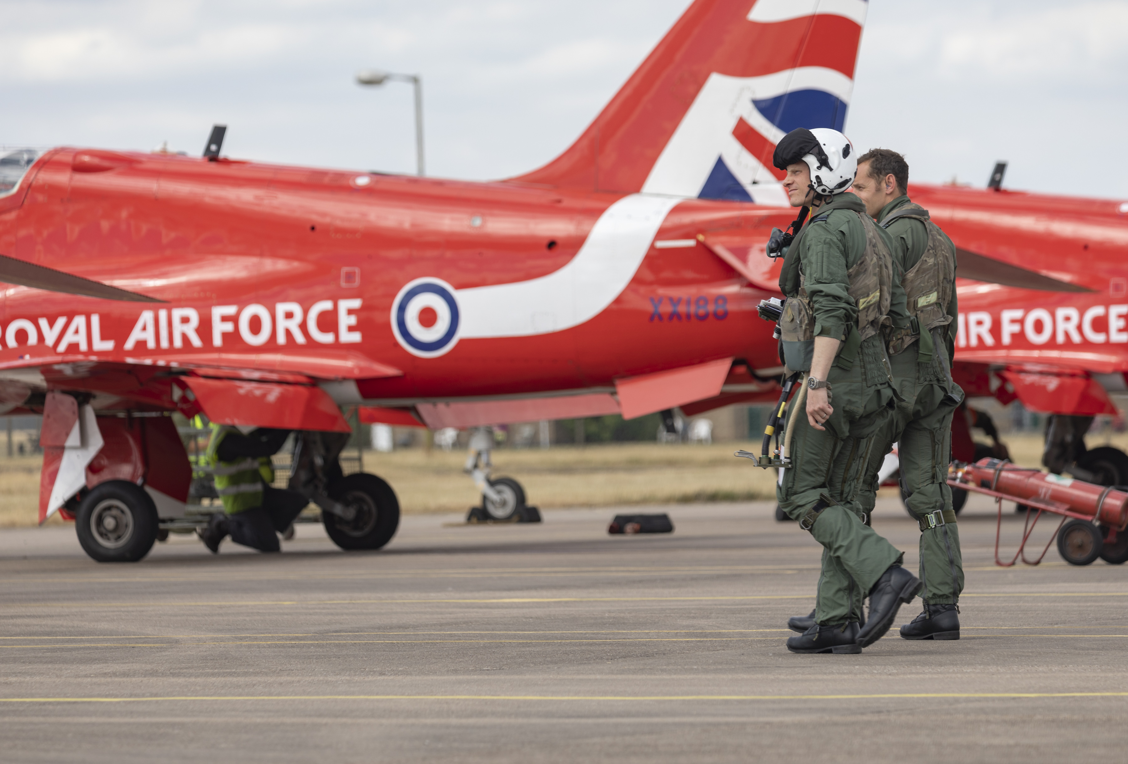 Image shows RAF Pilots walking on the airfield with Red Arrow Hawk aircraft.
